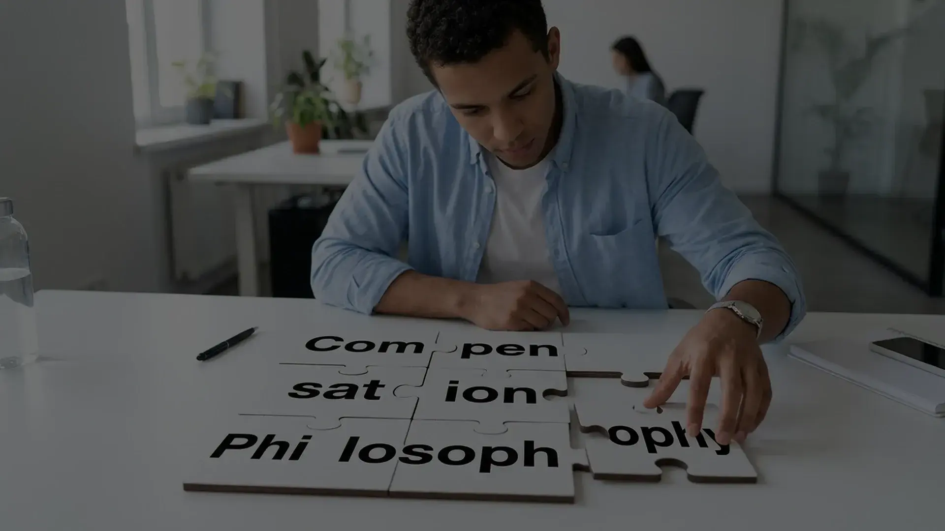 A man at a white desk fitting together jigsaw pieces printed with the words compensation philosophy.