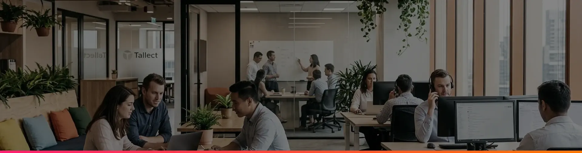 An open-plan office with people working at desks, a team at a whiteboard behind glass, and a Tallect sign on the wall.
