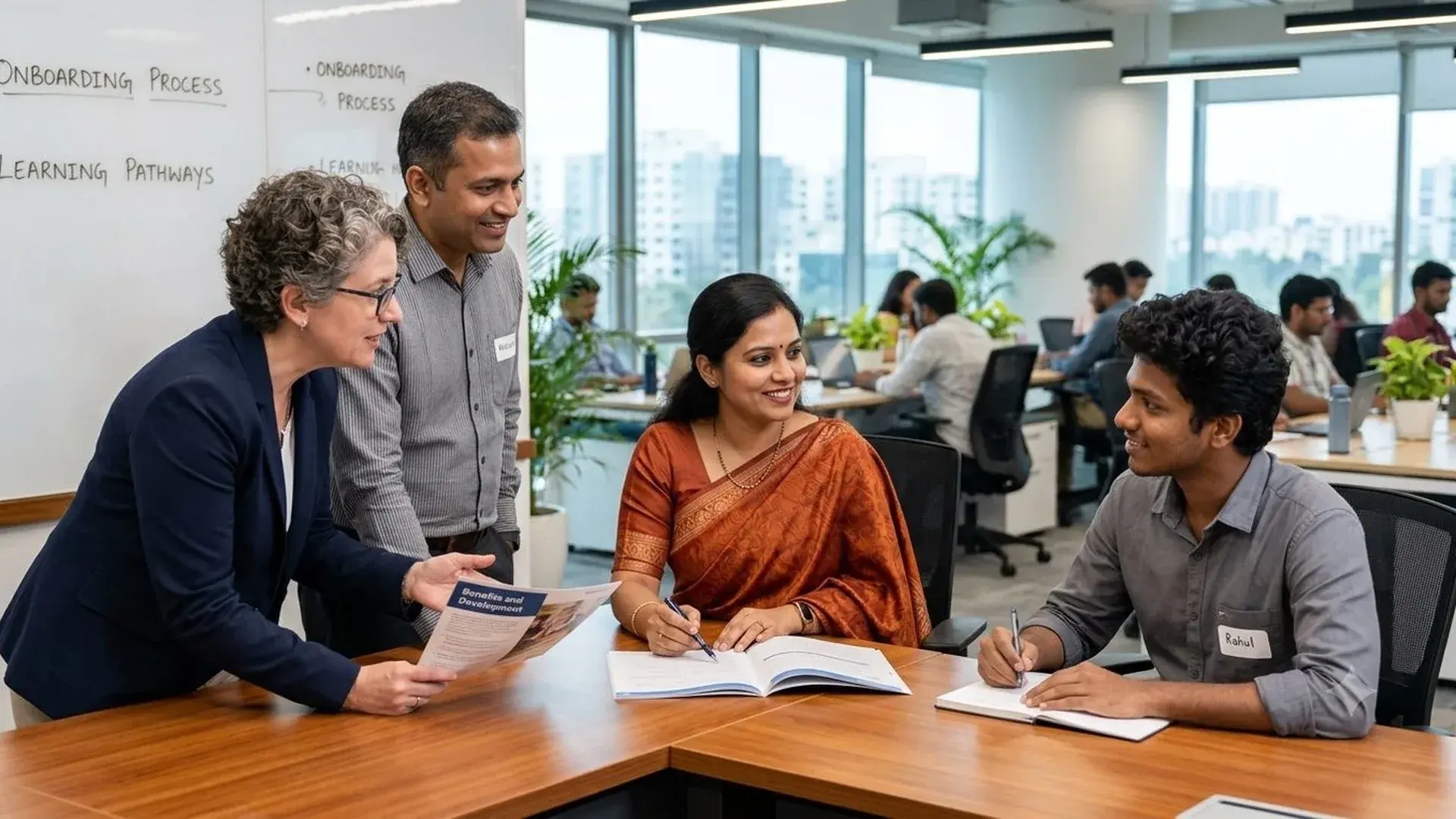 An HR leader shares a benefits and development brochure with three colleagues at a table in an open-plan office.