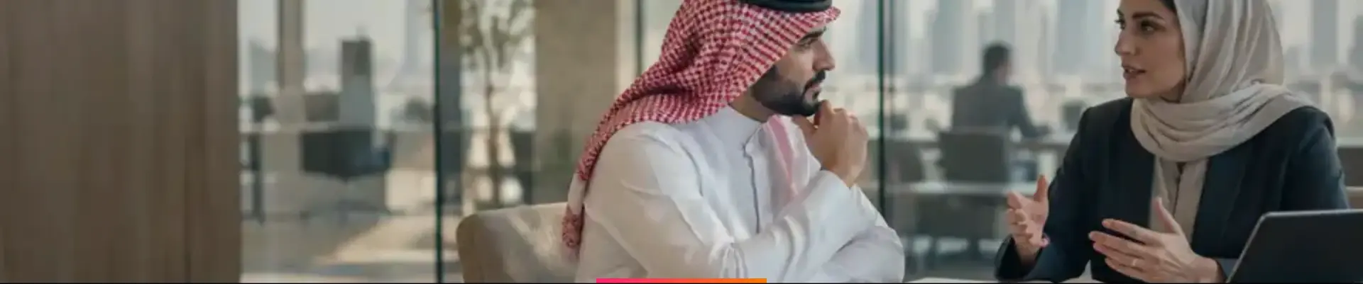 Two Saudi HR professionals in a focused one-to-one conversation in a glass meeting room